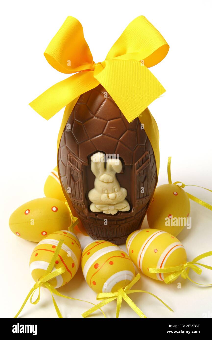 Easter party concept: Big chocolate egg with yellow ribbon, Easter bunny and decorative eggs, isolated on white background - Stock Image