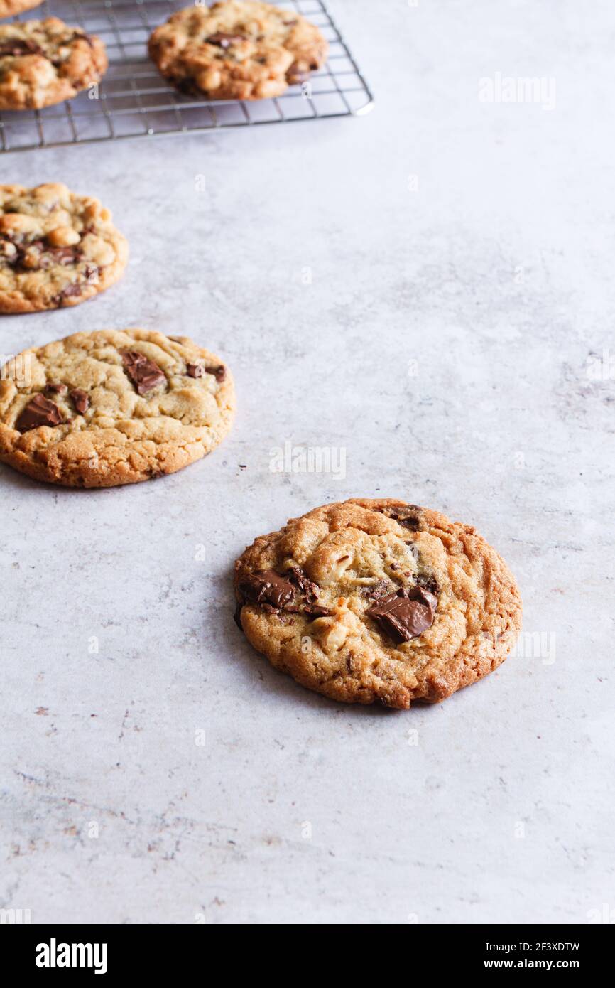 Freshly baked chocolate chip and hazelnut cookies with a few cooling on a wire rack in the background. Stock Photo