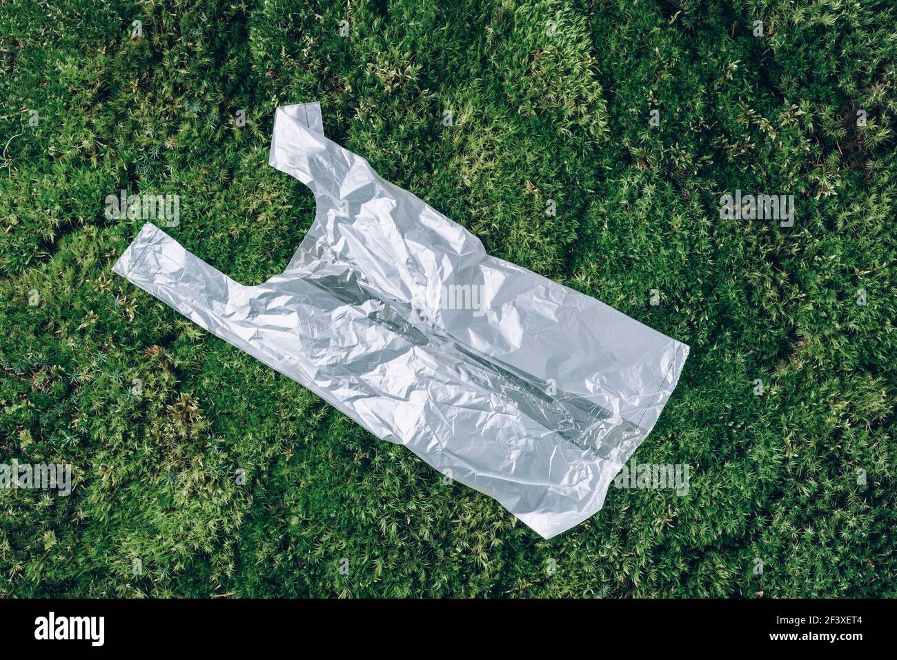 Pollution problem concept. Disposable plastic bag on green moss, grass background. Top view. Copy space. Environmental pollution problem. Garbage Stock Photo