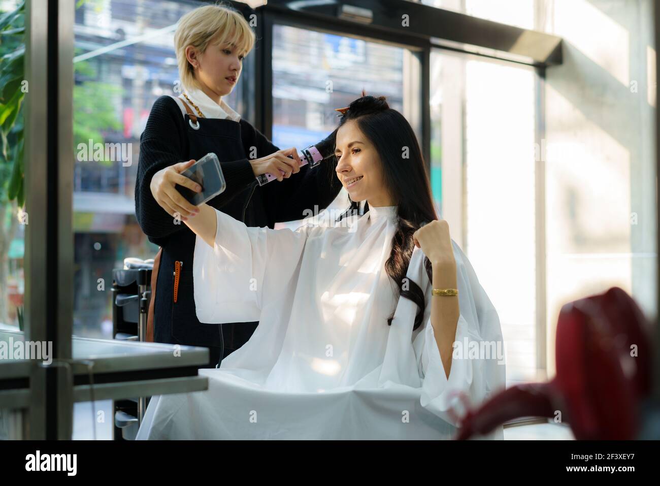 Image of a happy positive young beautiful woman client take a selfie with hair stylist in hair salon. Stock Photo