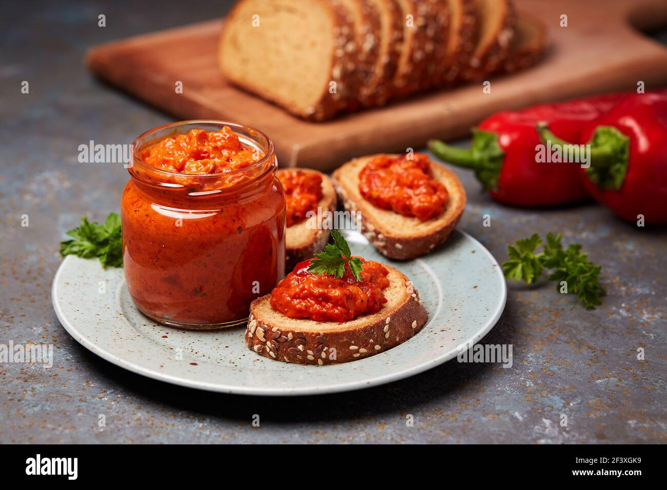 Ajvar (pepper mousse) in a jar and on a slices of bread. Ajvar - delicious dish of red peppers, onions and garlic. Stock Photo