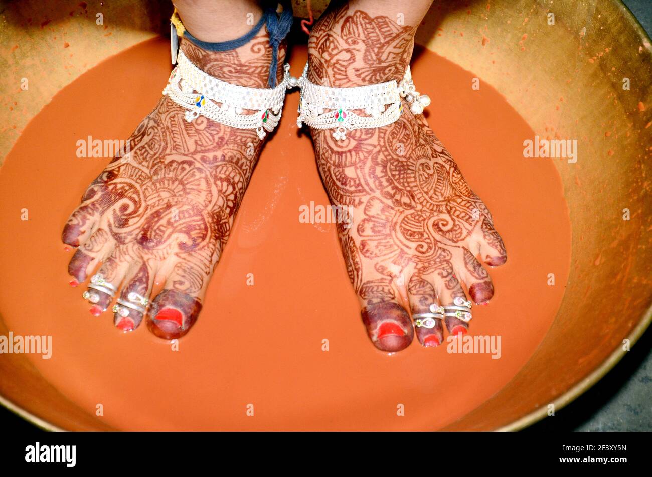 Griha Pravesh Ritual - Right feet of a Newly married Indian Hindu bride in Saree stepping in a plate filled with liquid kumkum before entering house f Stock Photo