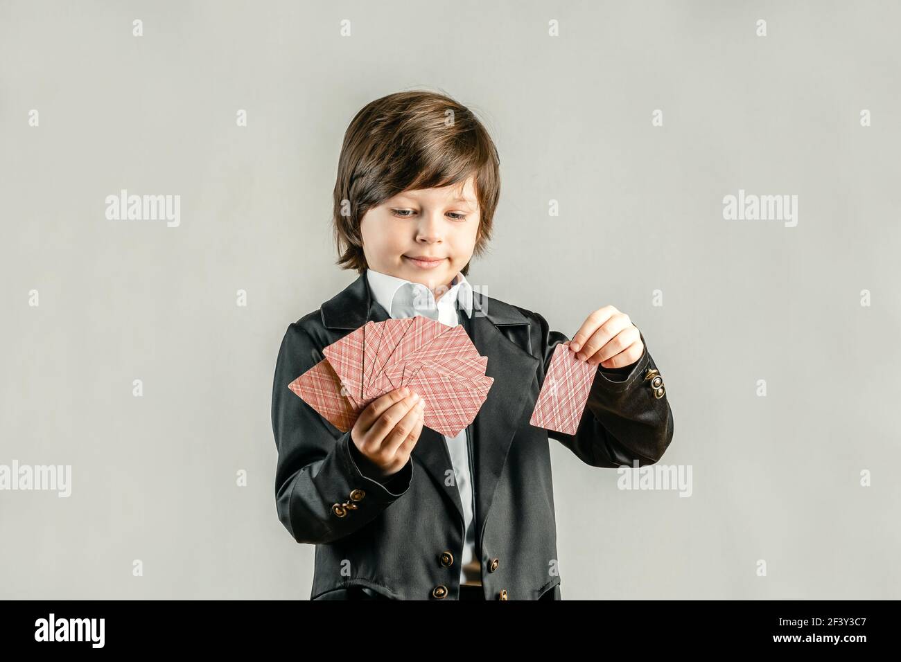 Young six year old boy wearing black suit and showing playing cards trick during illusionist