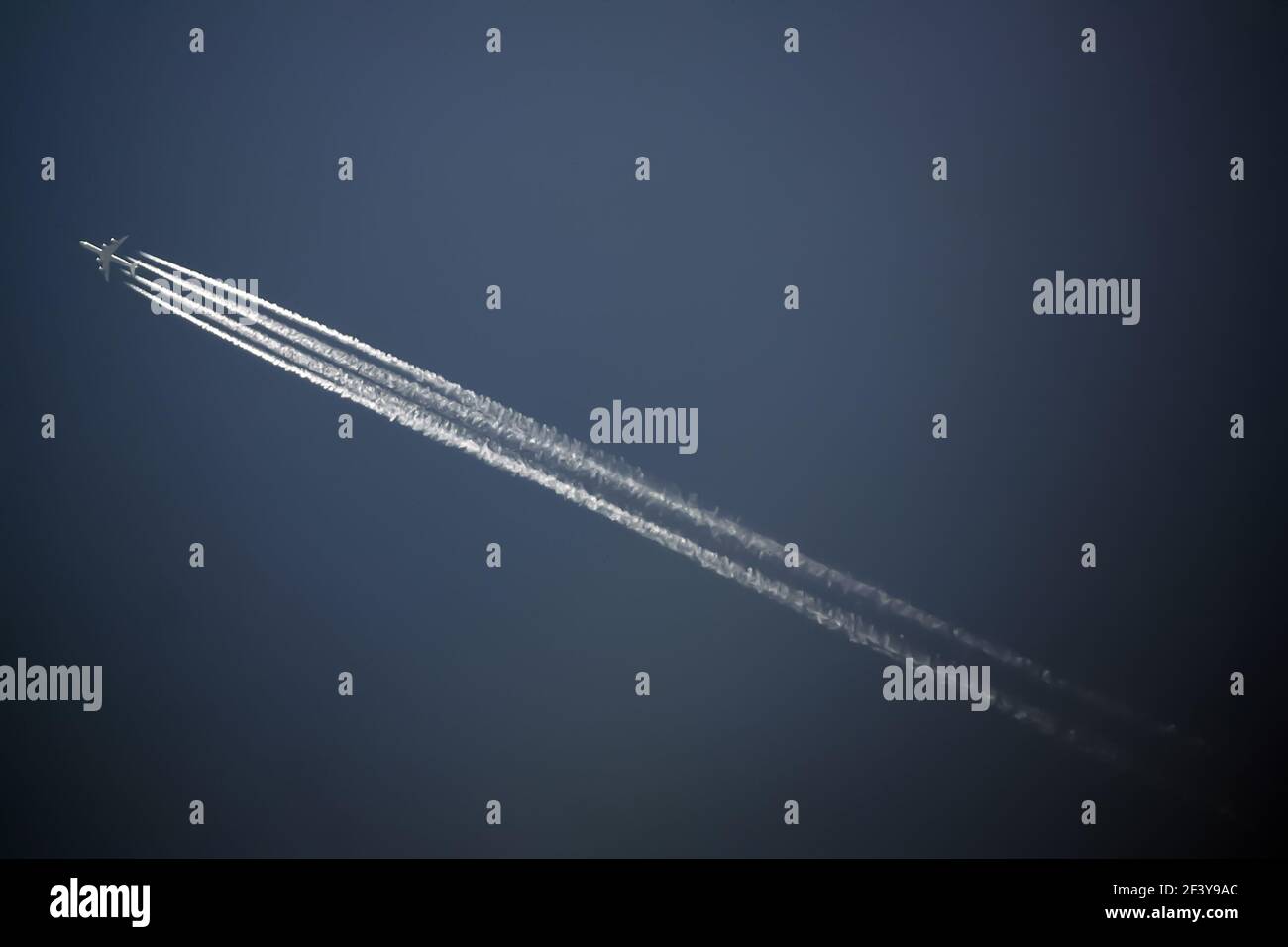 jet plane flies high in the blue sky, leaving behind a jet trail. Stock Photo