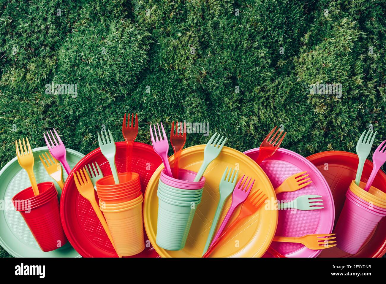 Colored plastic disposable tableware on green grass moss background