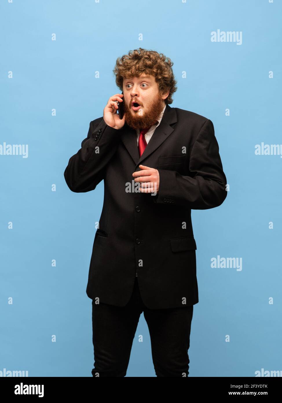 Portrait of young red-headed man in black suit isolated over blue ...
