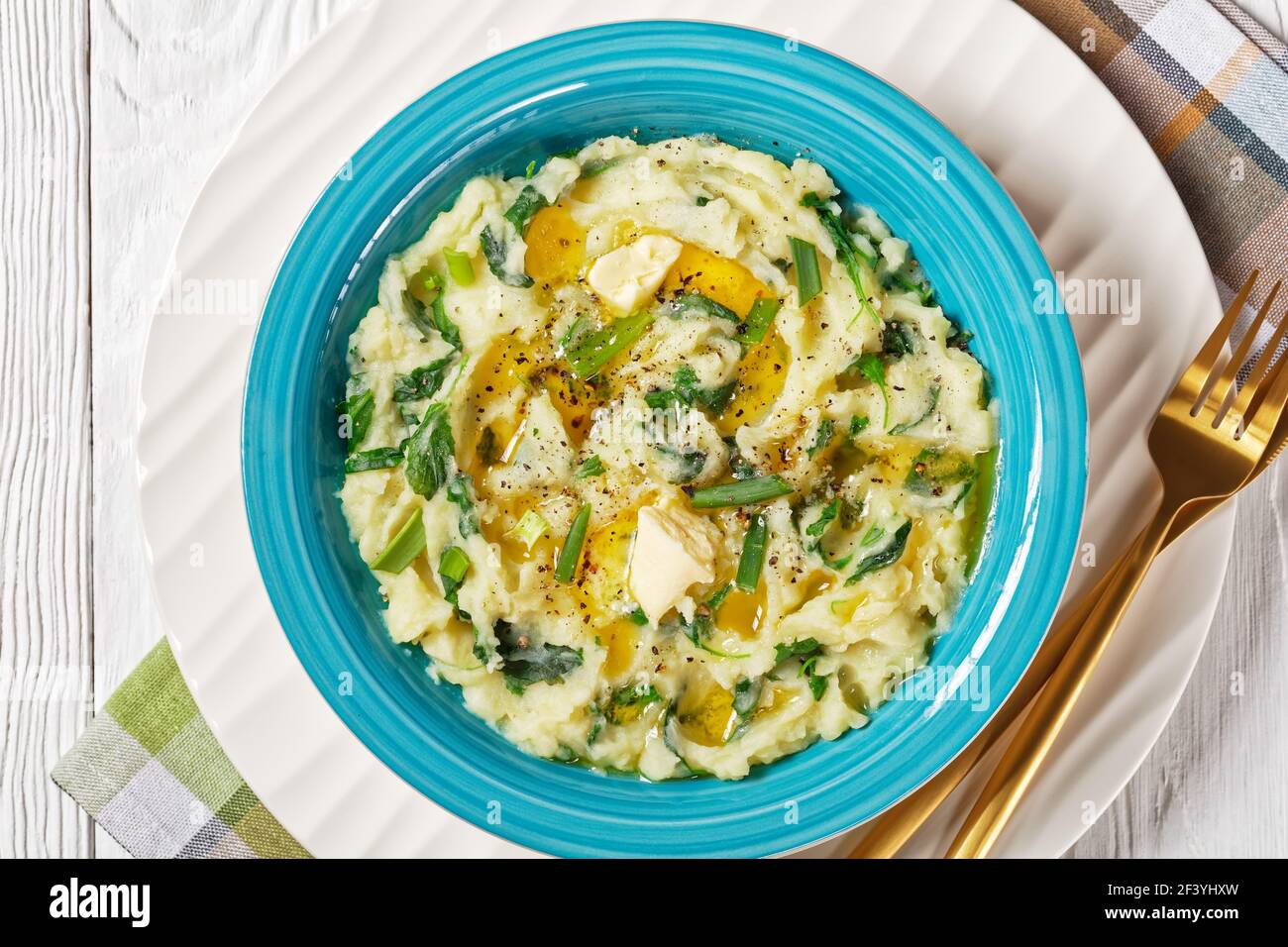 Irish colcannon traditional potato mash with kale, garlic, melted butter and spring onion served on a blue bowl with cutlery on a white wooden backgro Stock Photo