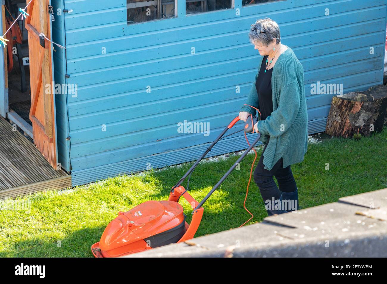 middle aged woman cutting the grass with a lawnmower Stock Photo