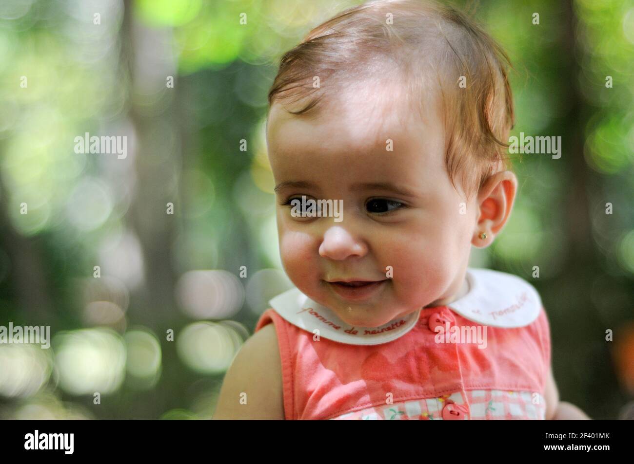 Six months old baby girl smiling outdoors.. Close-up portrait of six months old baby girl smiling outdoors with defocused background. Stock Photo