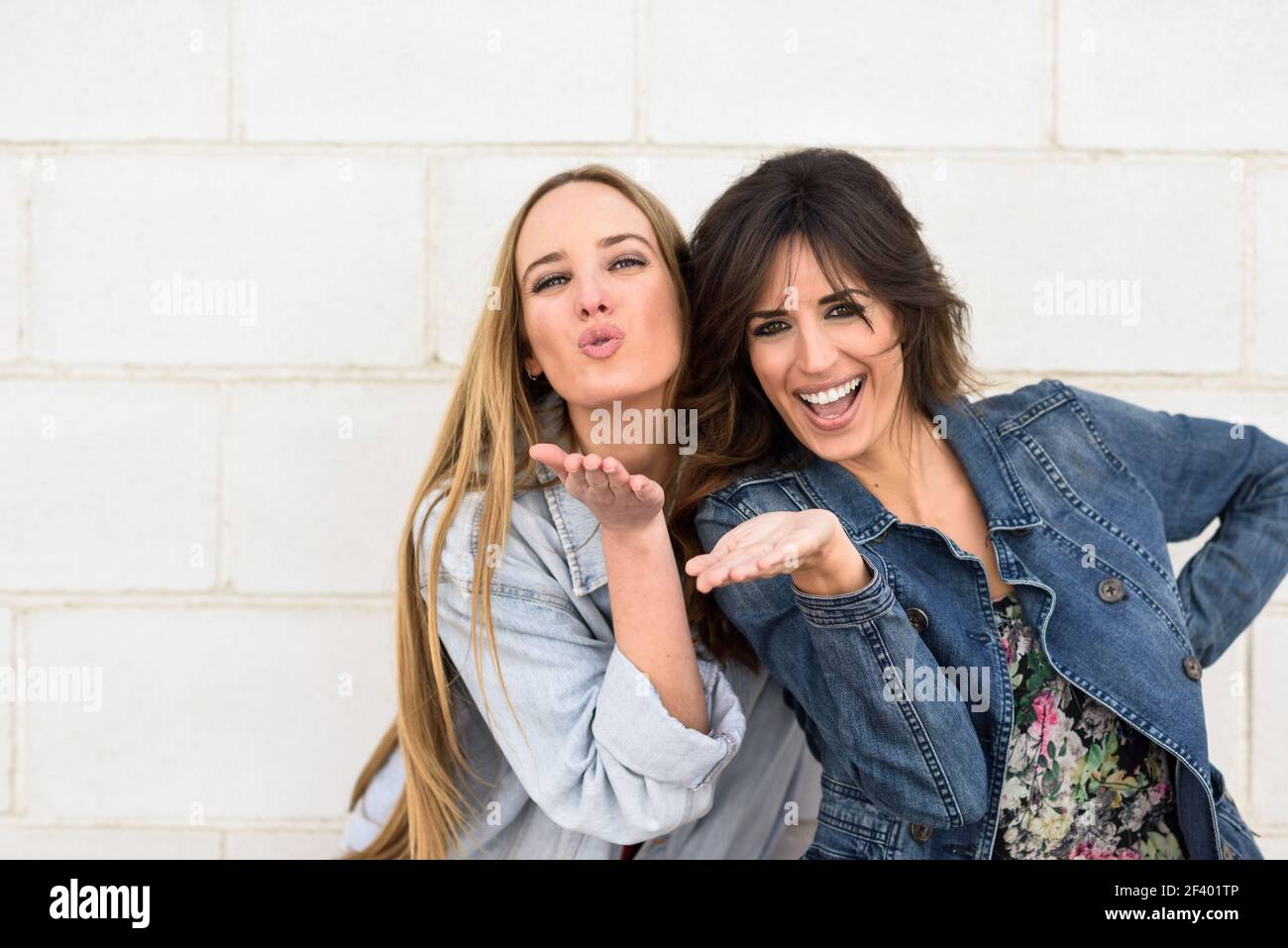 Two young women blowing a kiss on urban wall.. Two young women blowing a kiss on urban wall outdoors. Stock Photo