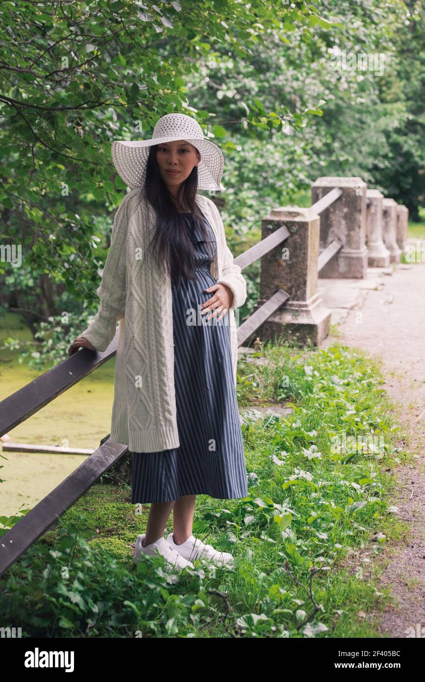 Young asian pregnant woman in white hat near bridge Stock Photo