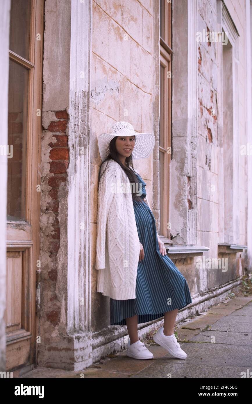Young asian pregnant woman in white hat near old building Stock Photo