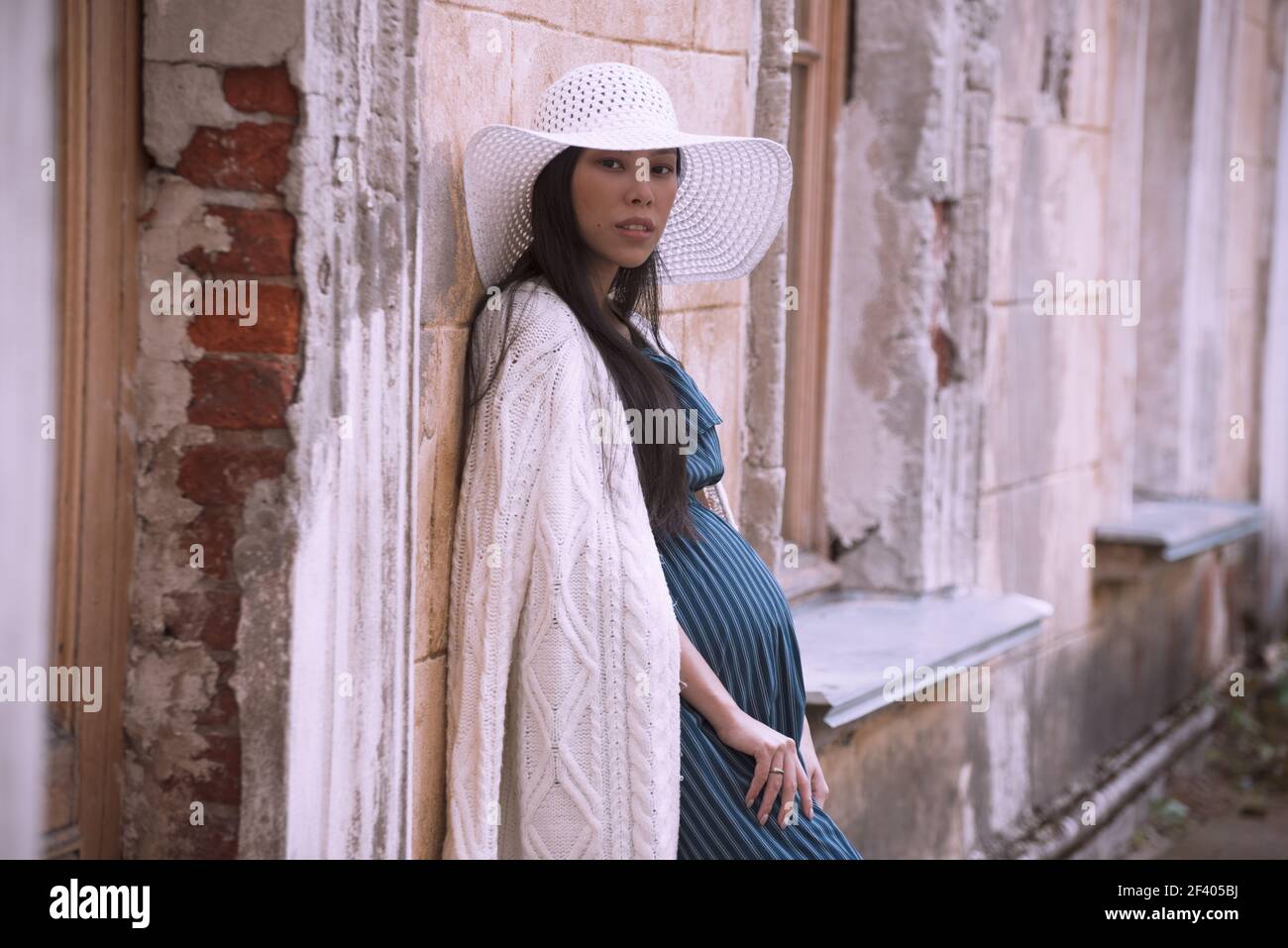 Young asian pregnant woman in white hat near old building Stock Photo