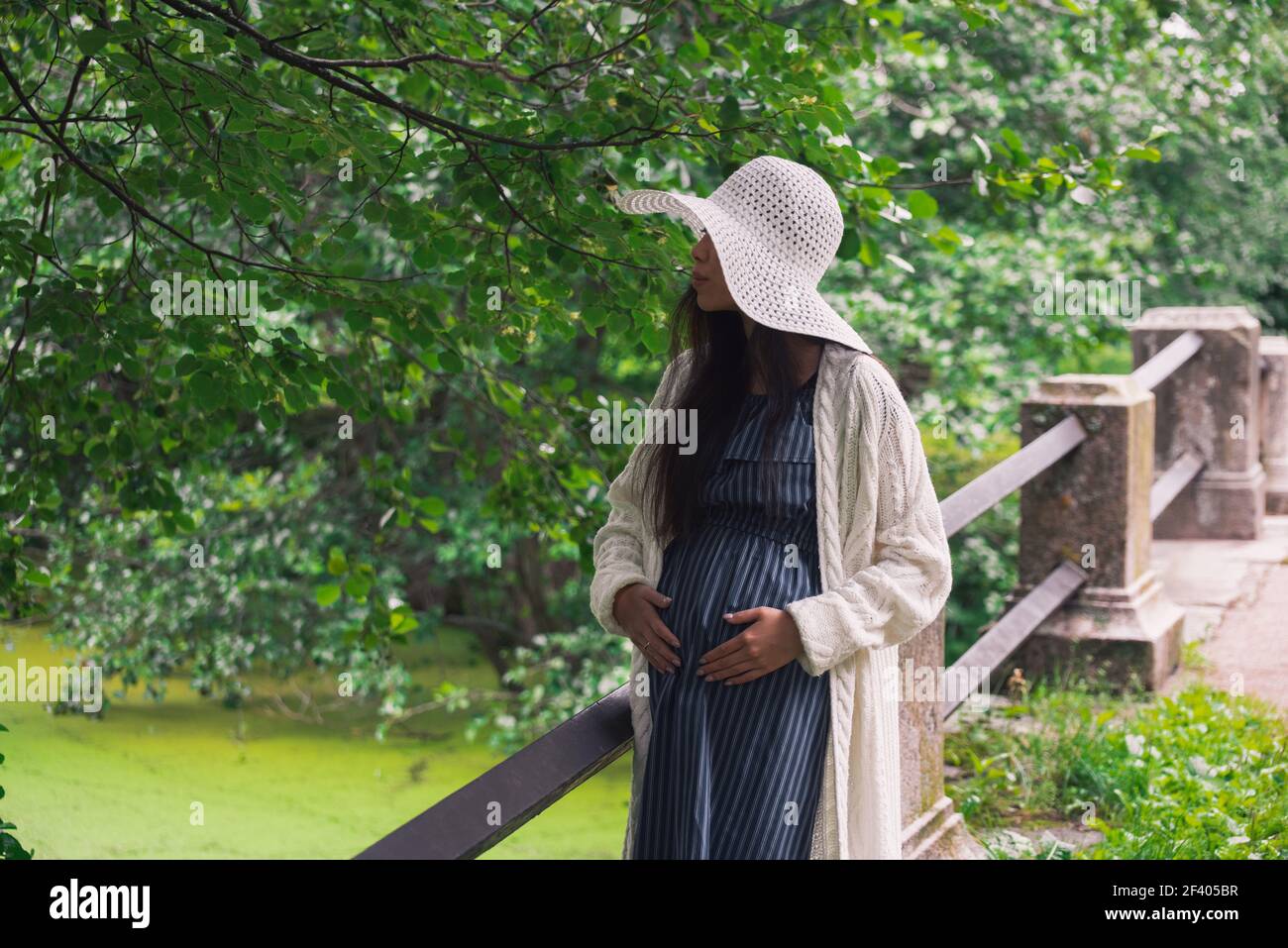 Young asian pregnant woman in white hat near bridge Stock Photo