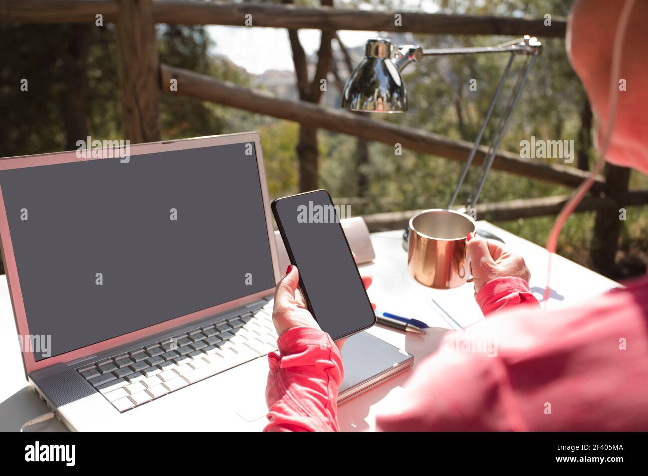 woman with phone in hand, outdoor influencer work table with computer, and office supplies. Mockups screens for text. Stock Photo