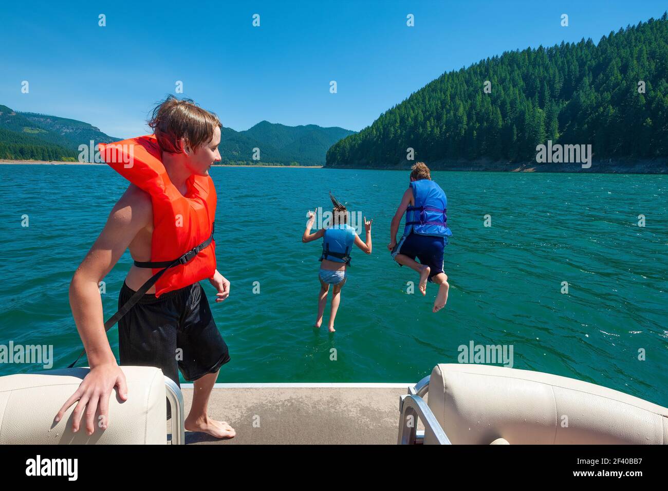 Teenage siblings jump off of boat deck into lake during summer vacation. Stock Photo