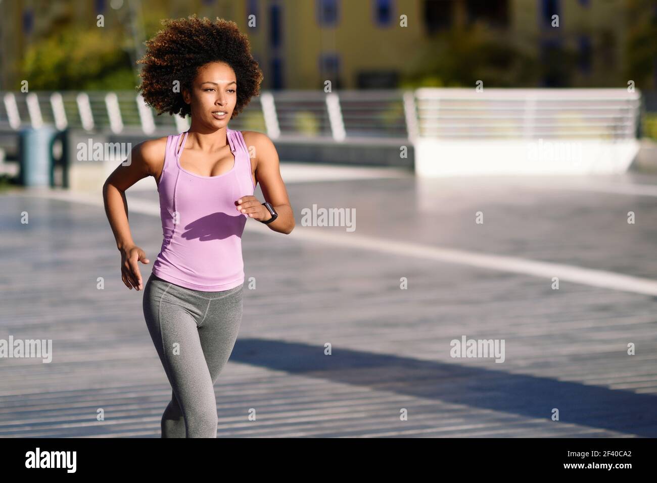 Black woman, afro hairstyle, running outdoors in urban road. Young female exercising in sport clothes. Stock Photo