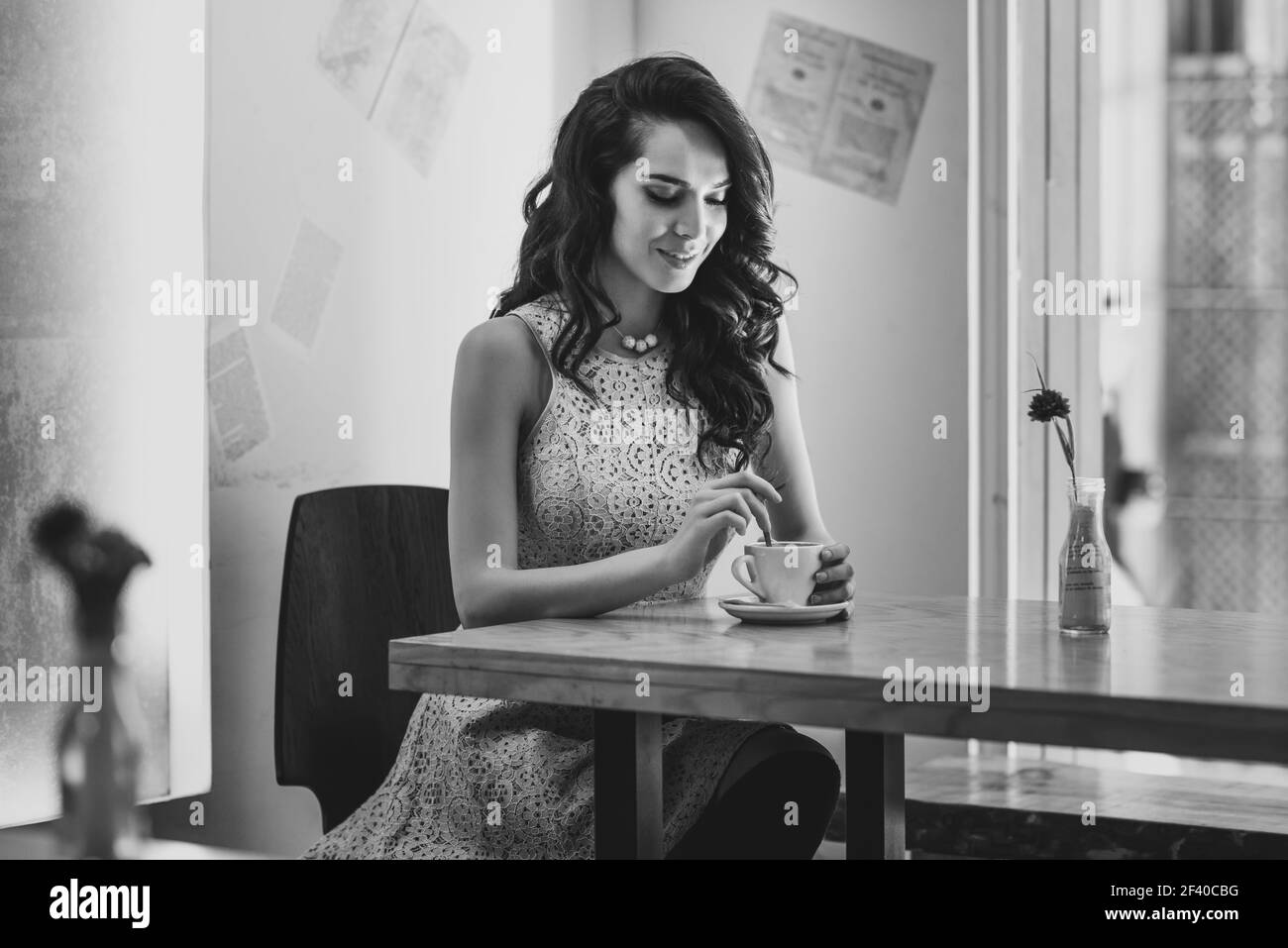 Young woman sitting indoor in trendy urban cafe moving teaspoon into coffee cup. Cool young modern caucasian female model in her 20s. Stock Photo