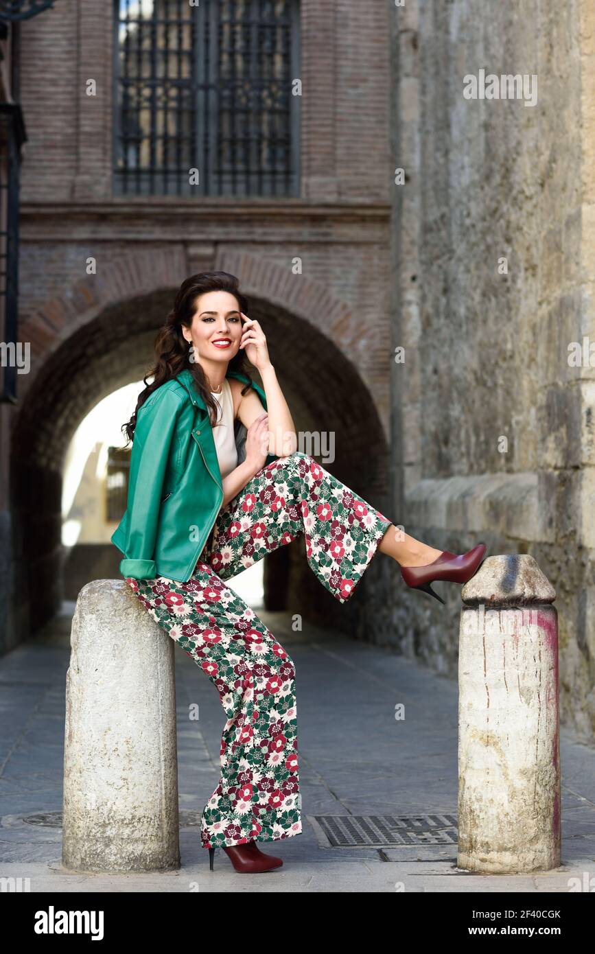 https://c8.alamy.com/comp/2F40CGK/young-brunette-woman-model-of-fashion-wearing-green-modern-jacket-and-flower-pants-pretty-caucasian-girl-with-long-wavy-hairstyle-smiling-female-with-red-lips-in-urban-background-2F40CGK.jpg