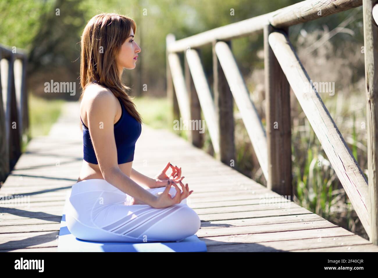 Young woman doing yoga in nature. Female wearing sport clothes in lotus figure. Stock Photo