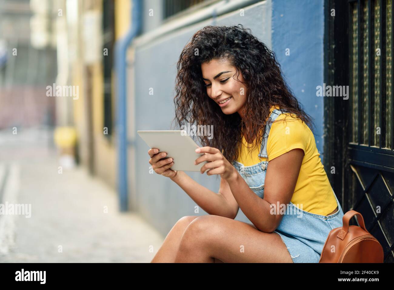Young Arab woman looking at her digital tablet outdoors. African girl wearing casual clothes inurban background. Curly hairstyle. Stock Photo