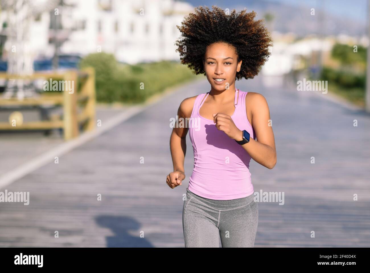 Black woman, afro hairstyle, running outdoors in urban road. Young female exercising in sport clothes. Stock Photo
