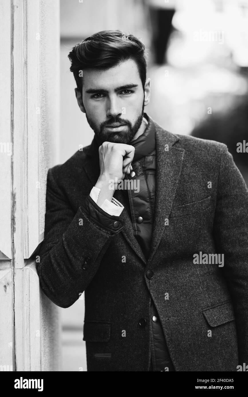 Young bearded man, model of fashion, in urban background wearing british elegant suit. Guy with beard and modern hairstyle in the street. Stock Photo