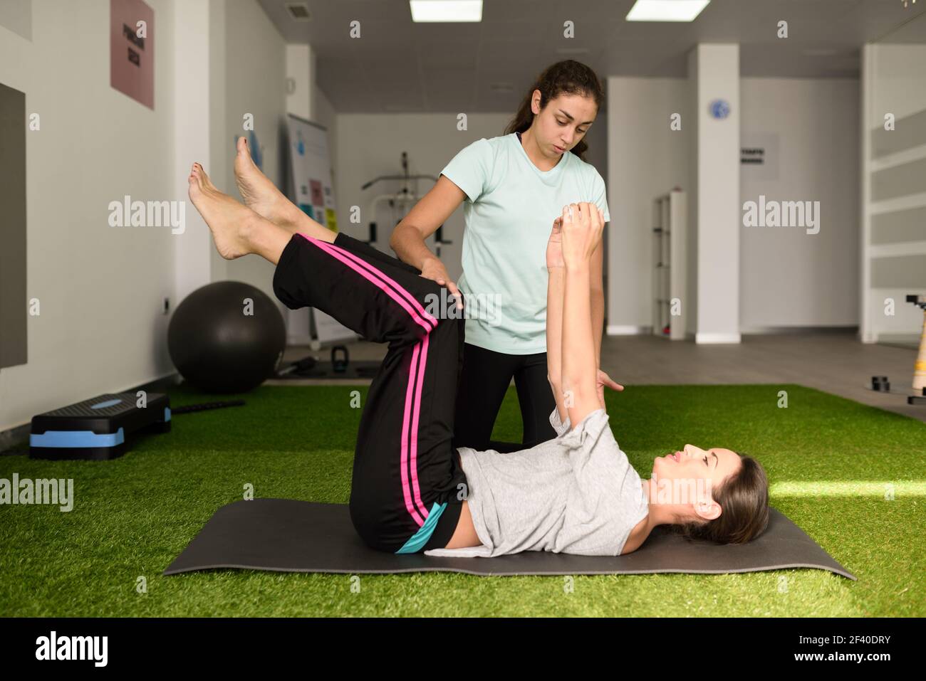 Physical therapist assisting young caucasian woman with exercise during rehabilitation in the gym at hospital. Female physiotherapist training a patient in physiotherapy center. Stock Photo