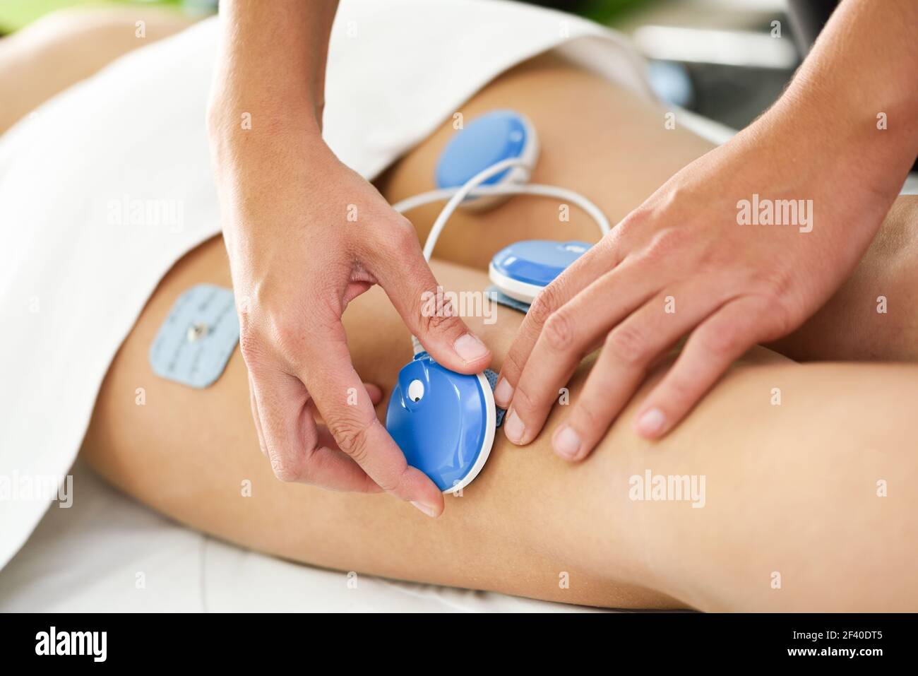 Physiotherapist applying electro stimulation in physical therapy to a young woman. Medical check at the leg in a physiotherapy center. Stock Photo