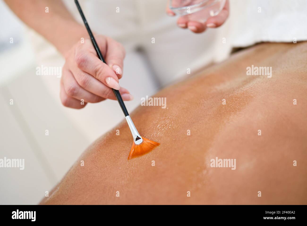 Woman receiving back massage treatment with oil brush in spa wellness center. Beauty and Aesthetic concepts. Stock Photo