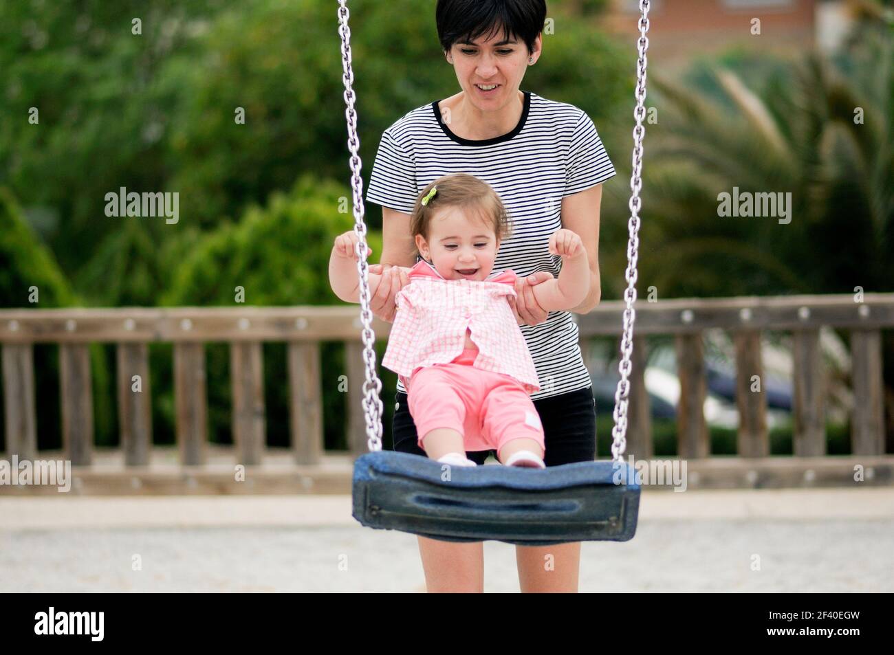 Mother swinging her little daughter on a swing in a playground Stock Photo
