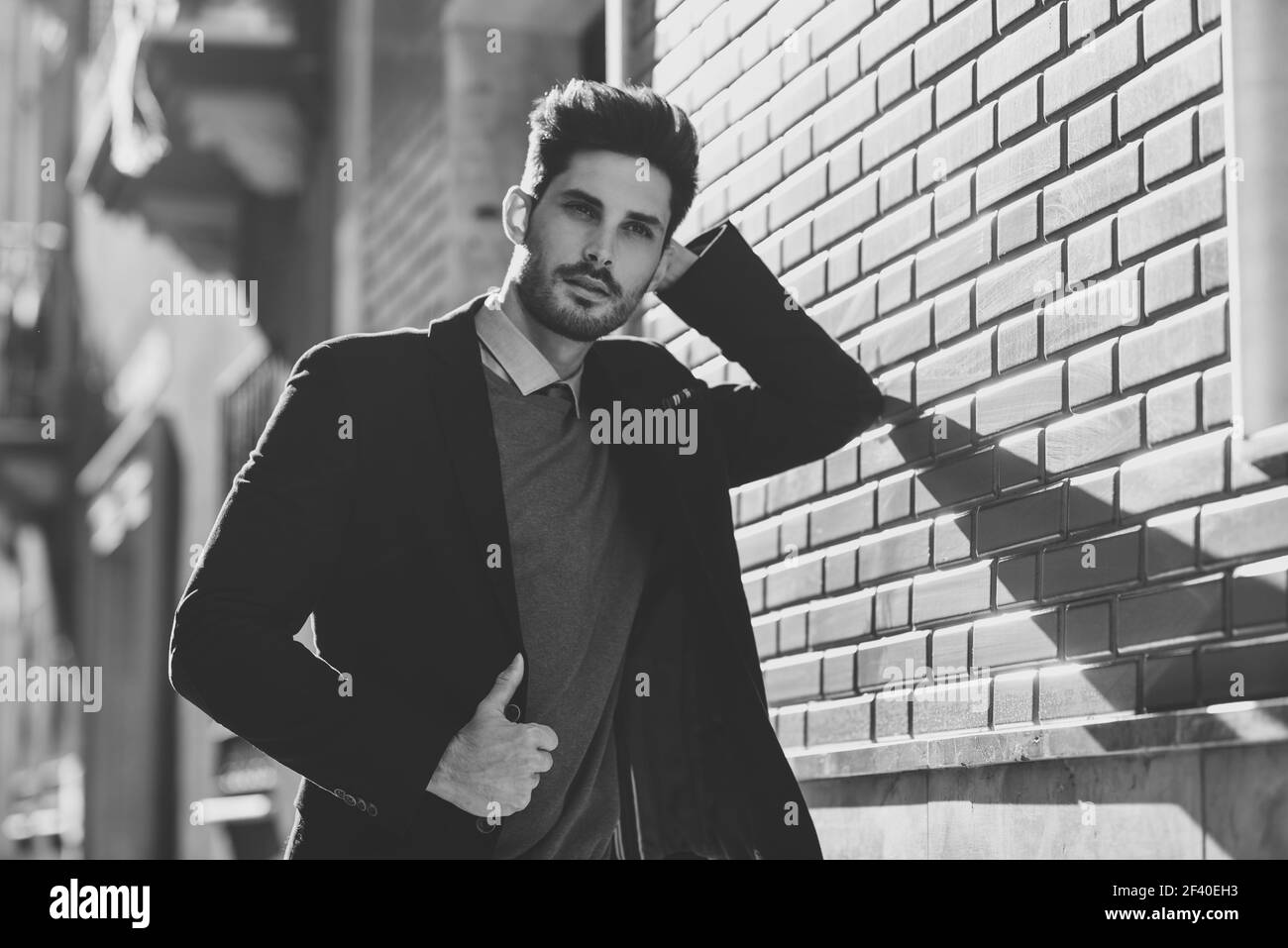 Attractive man in the street wearing british elegant suit. Young bearded businessman with modern hairstyle in urban background. Black and white photograph. Stock Photo