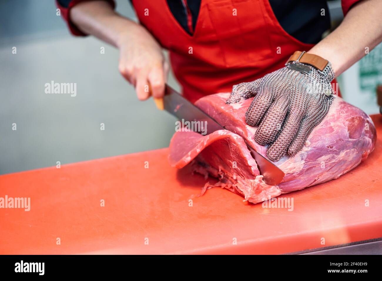 Female butcher cutting fresh meat in a butcher shop with metal safety