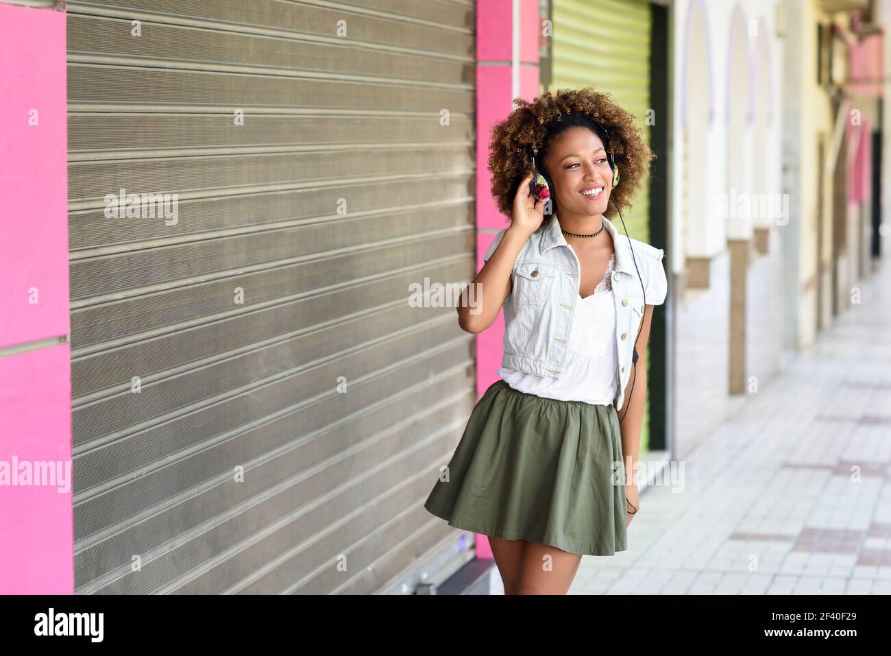 Young attractive black woman in urban street listening to the music with headphones. Girl wearing casual clothes with afro hairstyle Stock Photo