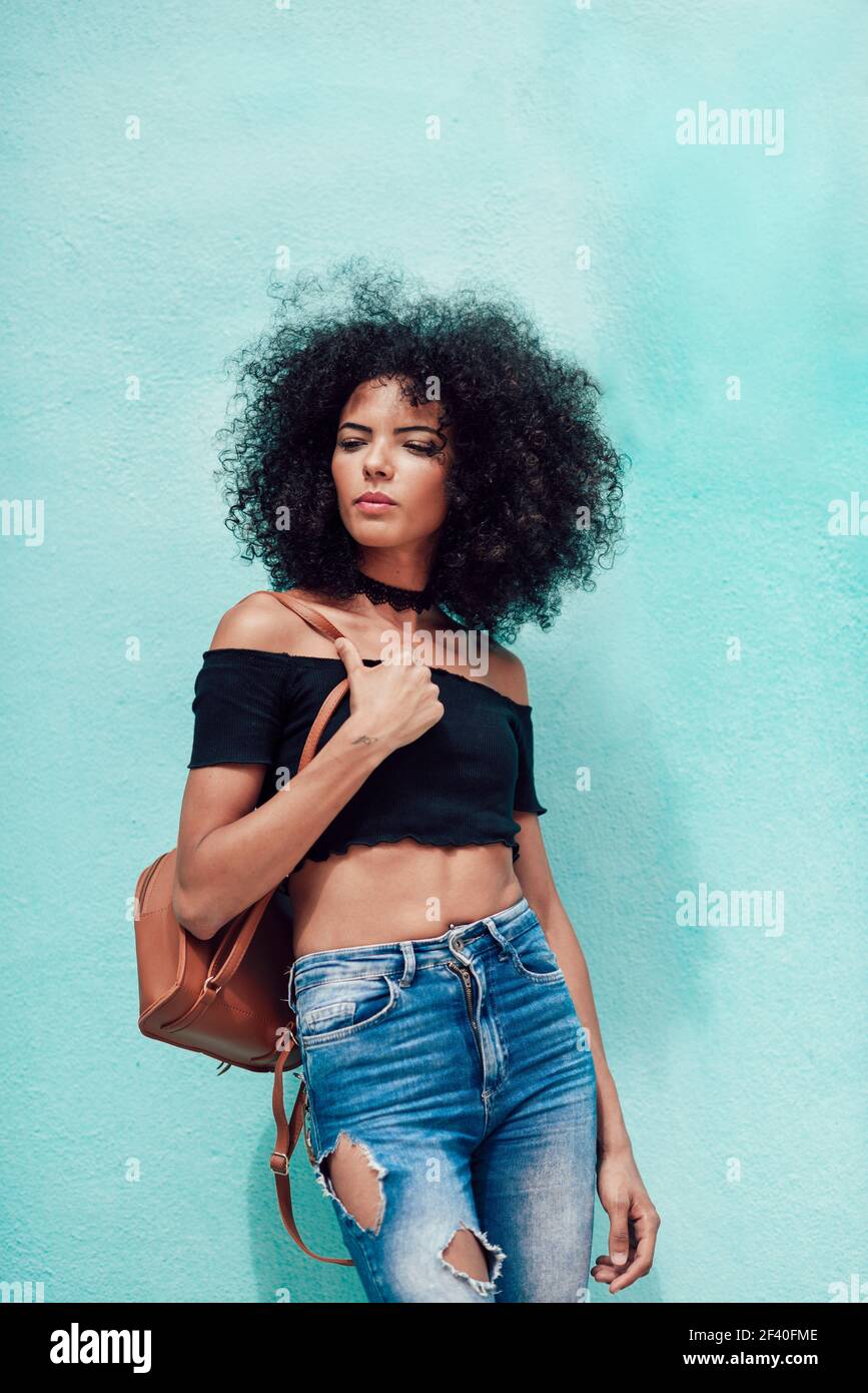 Young mixed woman with afro hair standing on the street. Female wearing casual clothes in urban background. Lifestyle concept Stock Photo