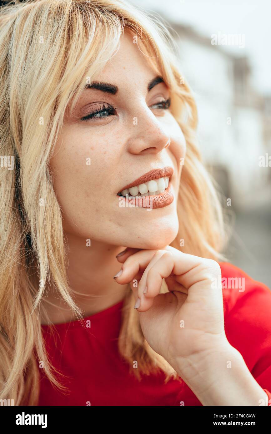 Close-up portrait of happy young blond woman sitting outdoors. Blonde girl with beautiful blue eyes.. Young blonde girl with beautiful blue eyes. Stock Photo