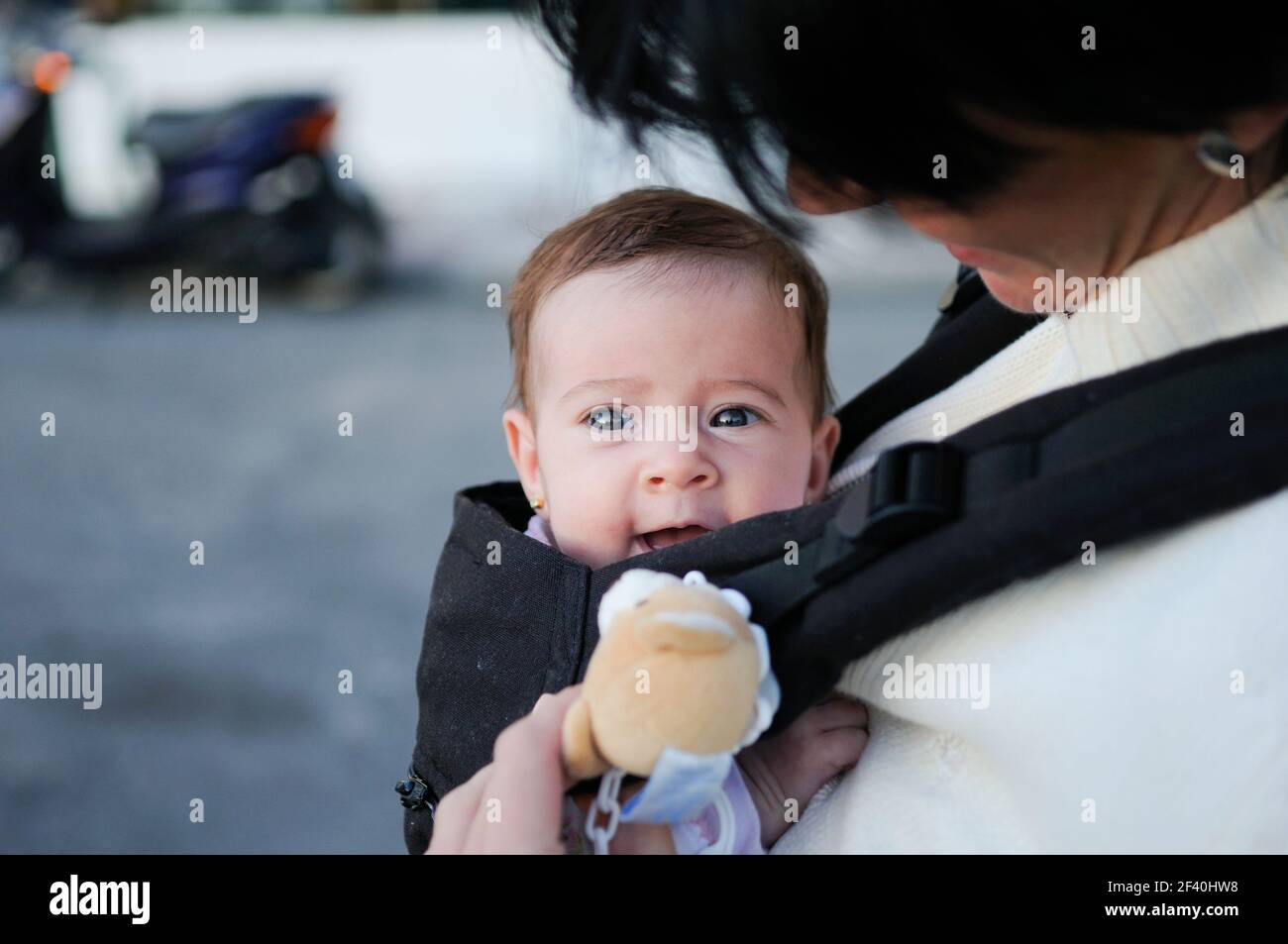 Mother carrying her baby girl in a baby carrier outdoors. Mother carrying her baby girl in a baby carrier Stock Photo