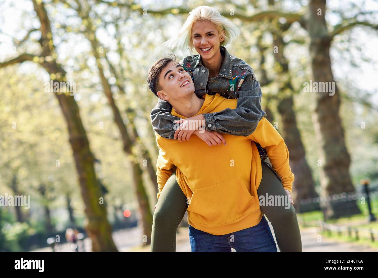 Funny couple in a urban park. Boyfriend carrying his girlfriend on piggyback. Love and tenderness, dating, romance. Lifestyle concept. Funny couple in a urban park. Boyfriend carrying his girlfriend on piggyback. Stock Photo
