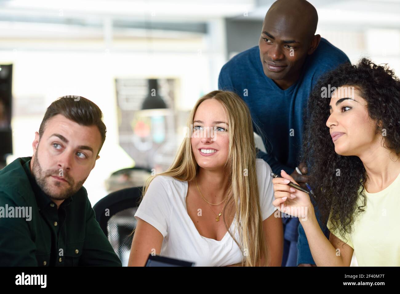 Four young people working together. Beautiful men and women in a business meeting wearing casual clothes. Multi-ethnic group..  Beautiful men and women working toghether wearing casual clothes. Stock Photo