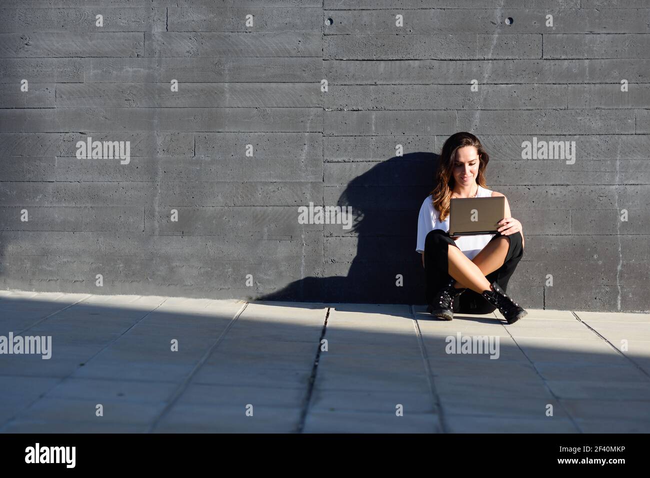 Young businesswoman working with her laptop computer sitting on the floor outdoors.. Middle-age businesswoman working with her laptop computer sitting on the floor. Stock Photo