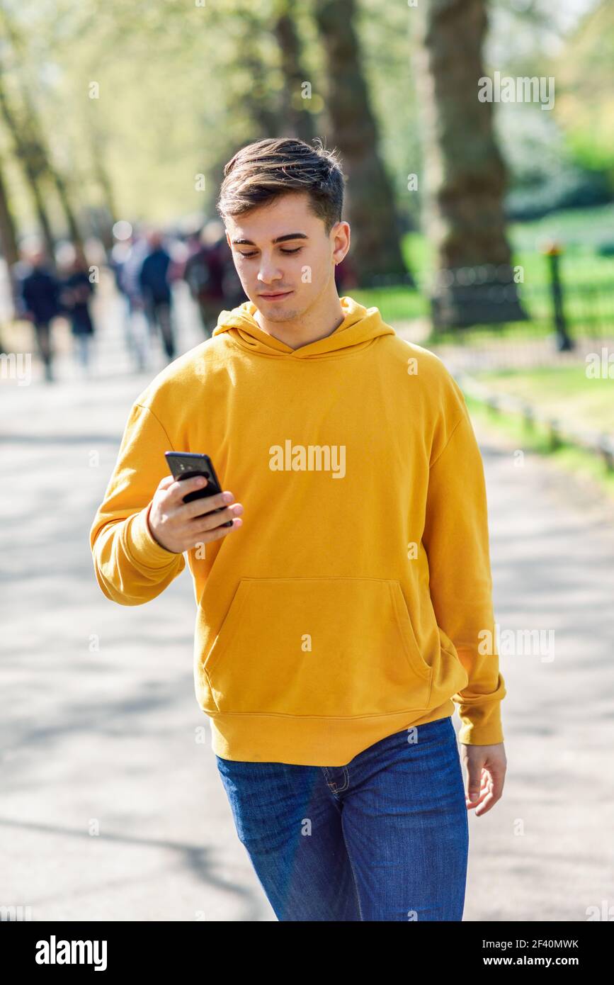 Young urban man using smartphone walking in street in an urban park in London, UK.. Young urban man using smartphone walking in street in an urban park in London. Stock Photo