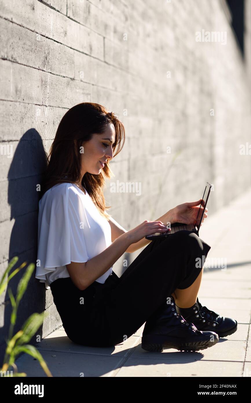 Middle-age businesswoman working with her laptop computer sitting on the floor outdoors.. Young businesswoman working with her laptop computer sitting on the floor. Stock Photo