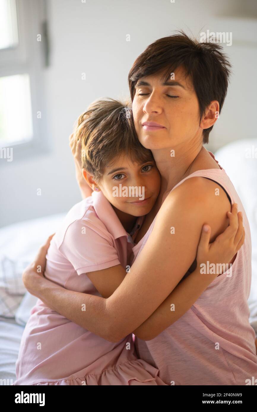 Beautiful young woman and her charming little daughter are hugging on the bed.. Beautiful young woman and her charming little daughter are hugging. Stock Photo