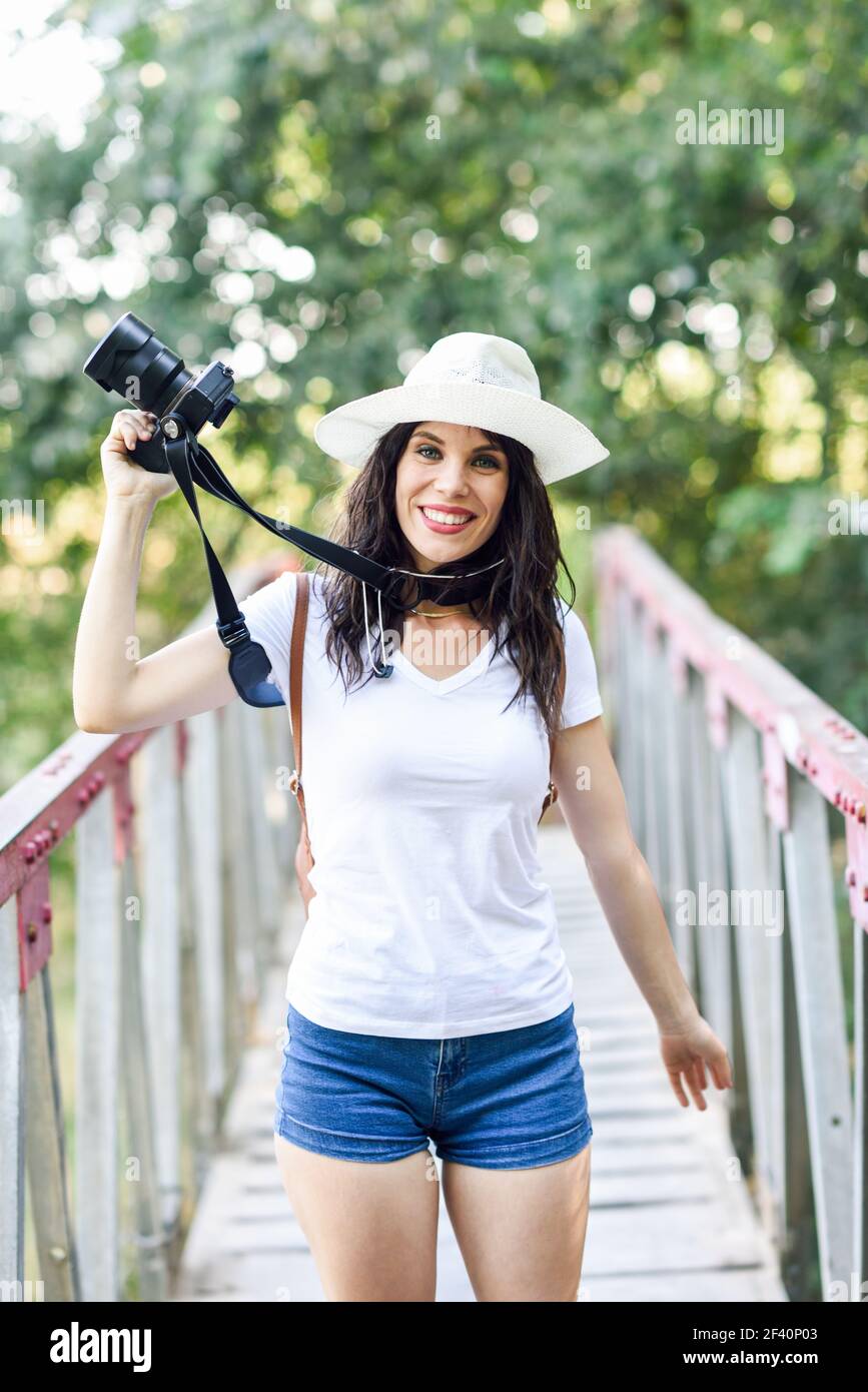 Beautiful hiker young woman taking photographs with a mirrorless camera, wearing straw hat, hiking in the countryside.. Hiker woman taking photographs with a mirrorless camera Stock Photo