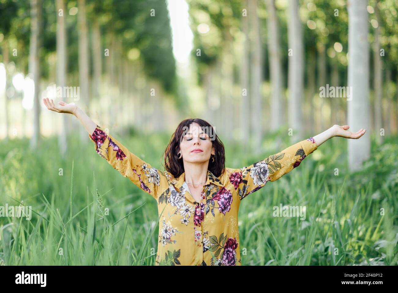 Enjoying the nature. Young woman arms raised enjoying the fresh air in green forest. Female with eyes closed.. Woman arms raised enjoying the fresh air in green forest. Stock Photo