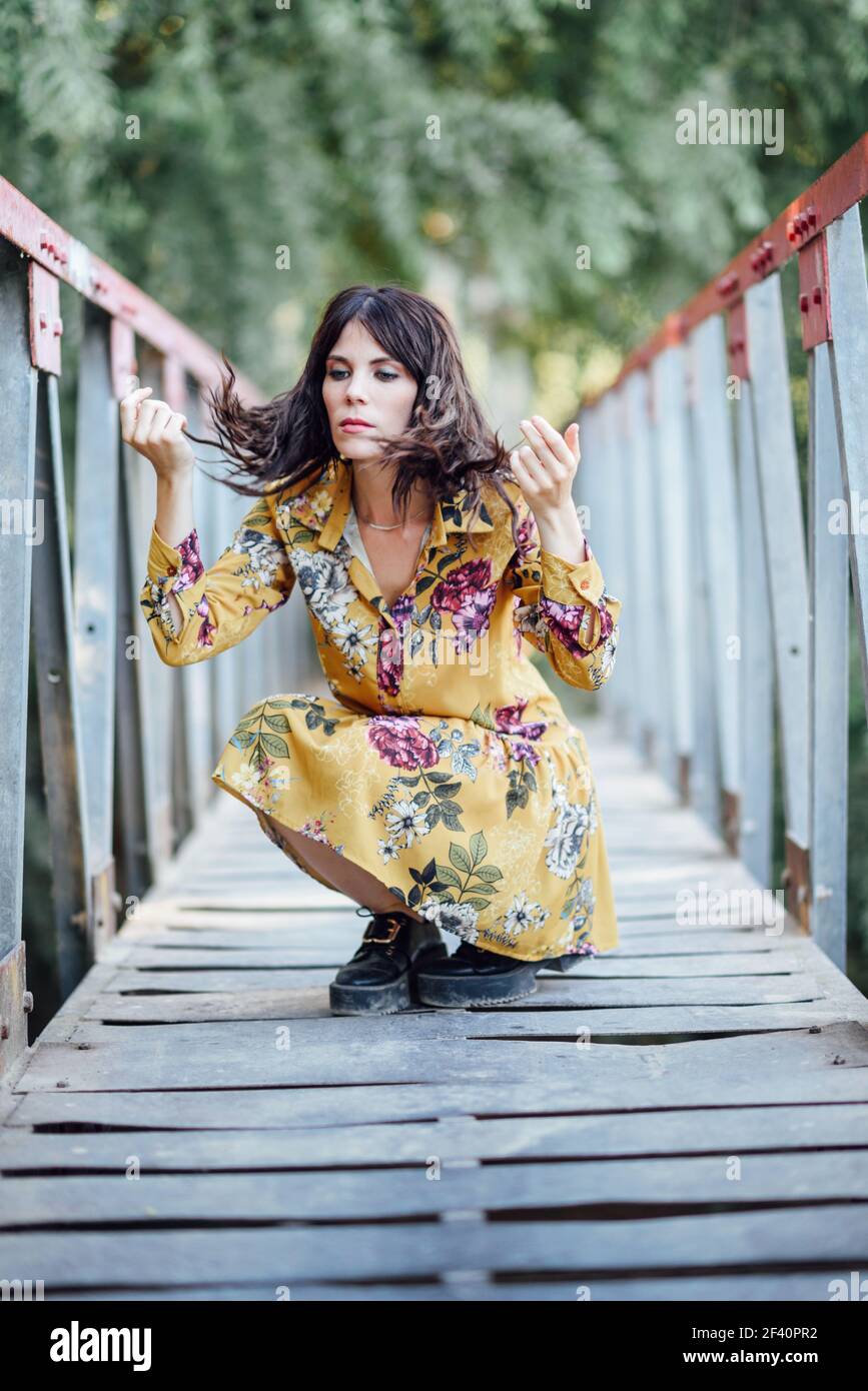 Young woman, wearing flowered dress, hiking in the countryside. Female having fun on a rural bridge.. Woman wearing flowered dress hiking in the countryside Stock Photo