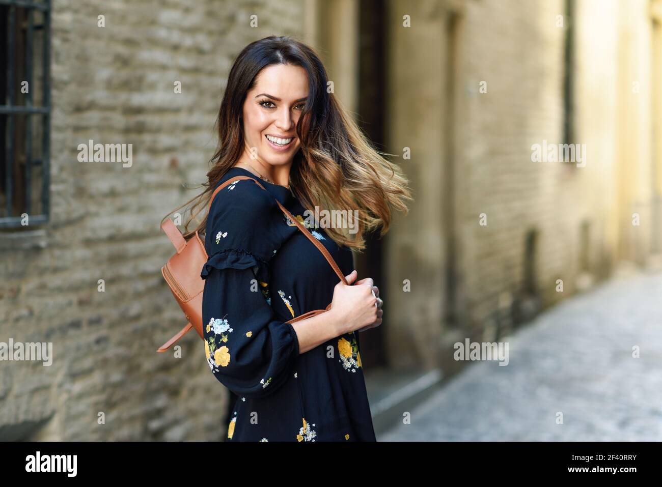 Young woman moving her long hair in urban background. Female in casual clothes with care hairstyle in Granada, Andalusia, Spain.. Young woman moving her long hair in urban background. Stock Photo