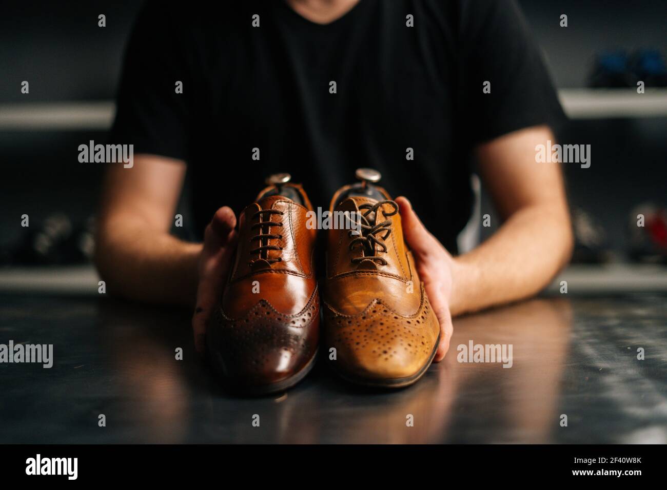 Close-up hands of male shoemaker holds old light brown leather shoe and repaired shiny shoes after restoration working. Stock Photo