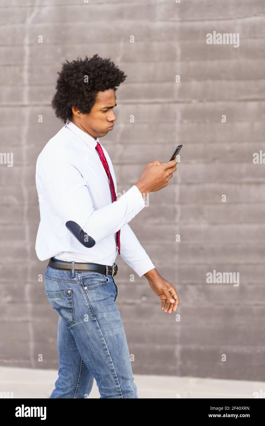Concerned Black Businessman using his smartphone walking down the street.. Concerned Black Businessman using his smartphone outdoors Stock Photo