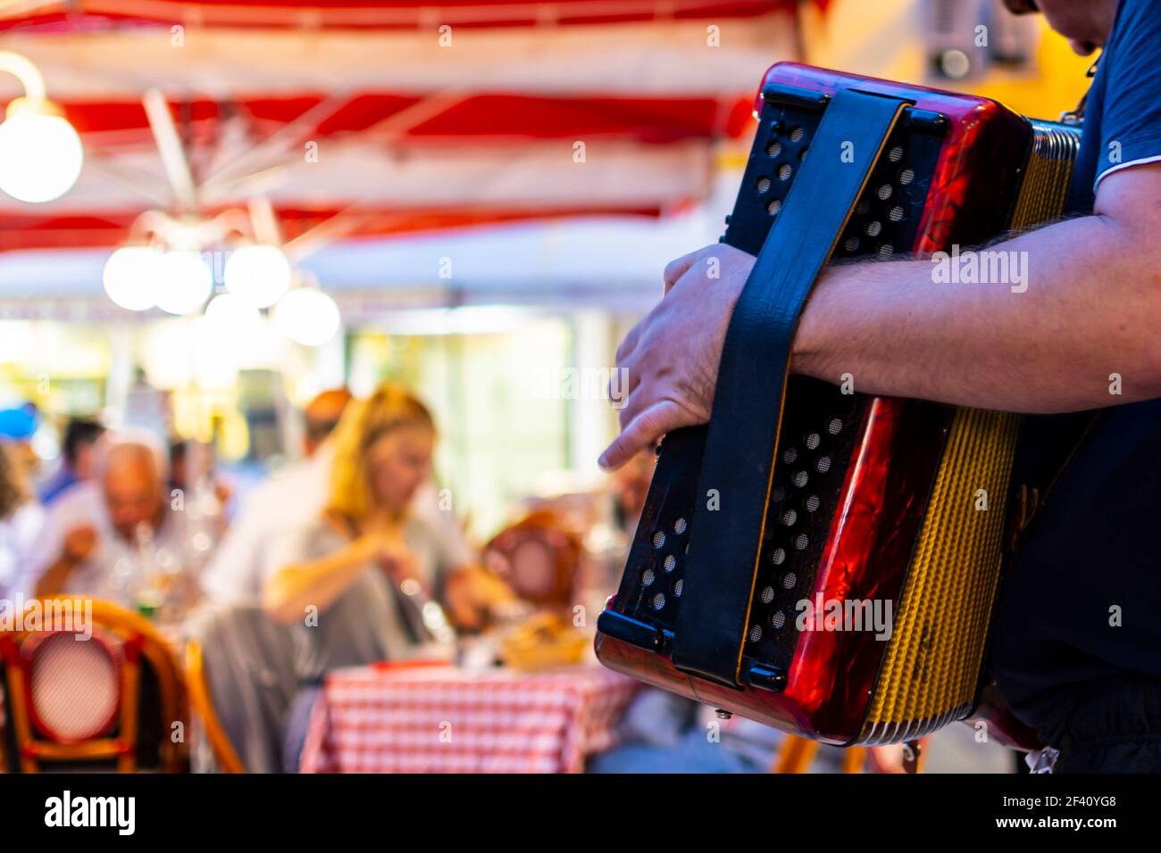 An accordion player musician plays for diners at an outdoor Italian restaurant in the center of Old Town Nice, France. Stock Photo